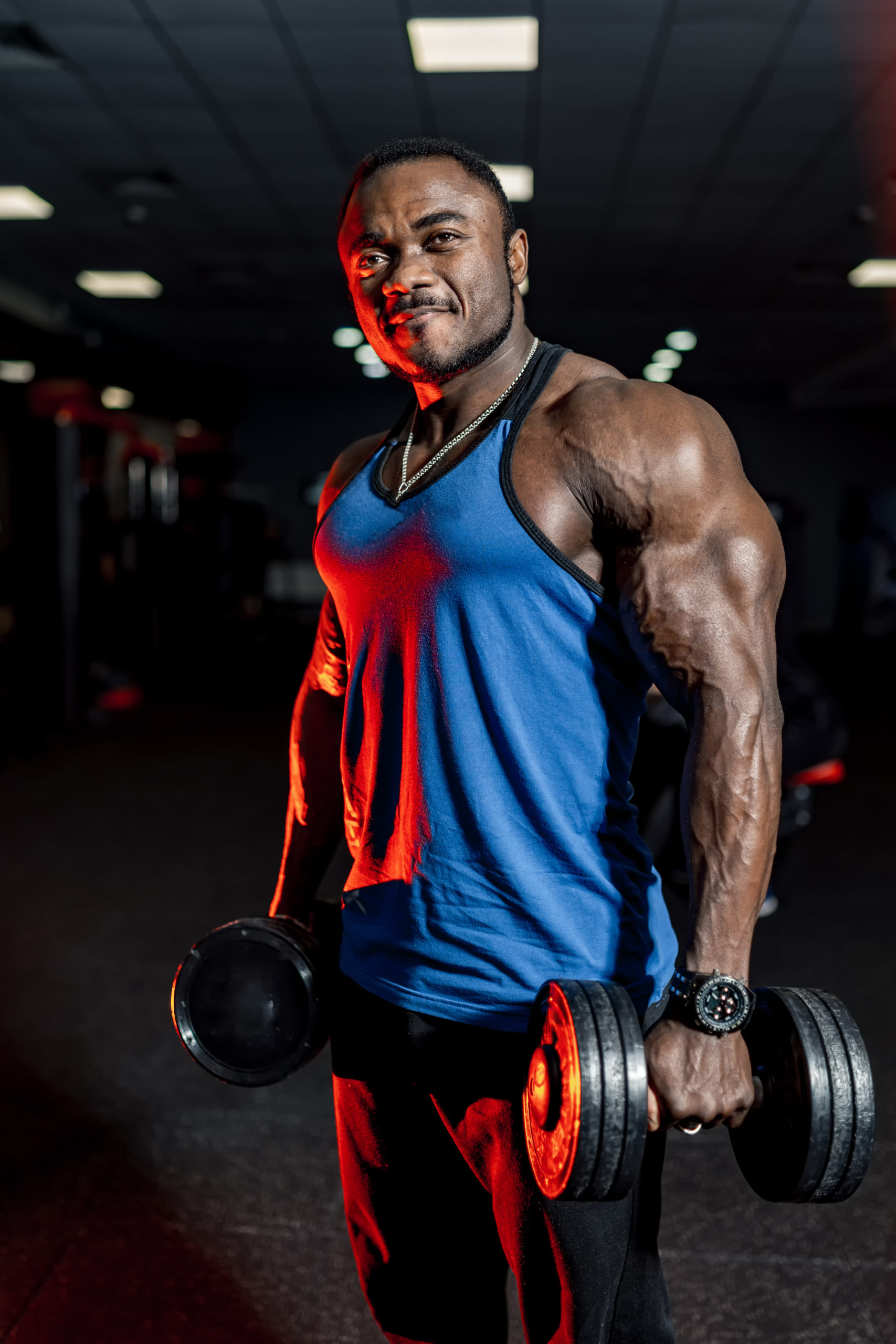 Male bodybuilder working out with a heavy dumbbell. Modern gym background. Blue shirt.
